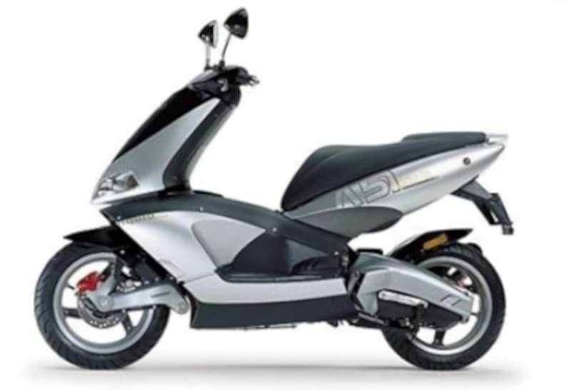 <div class='descrGalleryTitle'>Area 51</div><div class='descrGalleryText'><p>L'Aprilia Area 51, lanciato nel 1998, è uno scooter che <b>ha fatto parlare di sé per il suo design avveniristico </b>e le soluzioni tecniche innovative. Con un nome ispirato alla famosa base militare statunitense che ospiterebbe al suo interno carcasse di UFO, l'Area 51 si distingue per le sue linee anticonvensionali e l’avantreno che non sfrutta una tradizionale forcella telescopica, bensì un <b>monobraccio oscillante. </b>E se un monobraccio è già una complicazione, due è un incubo: tanto è vero che per qualche errore progettuale i prototipi dell'Area 51 non risultarono particolarmente stabili, e l'unica soluzione risultò quella <b>di montare il motore e altri componenti disassati </b>(cosa che all'epoca ovviamente non si seppe)<b>. </b>Non lo aiutò il design troppo audace, accompagnato da grafiche sobrie e pulite: per quanto ancora bellissimo e attuale a distanza di 25 anni, all’epoca però non incontrò il gusto del pubblico, più attratto dalle linee sportive. <b>Il vero problema dell’Area 51 si chiamava infatti SR 50,</b>&nbsp;lo scooter sportivo di casa Aprilia già iper affermato sin dai primi Anni 90 e rispetto al quale, per via delle scelte tecniche, <b>l'Area 51 costava sensibilmente di più.&nbsp;</b>L’SR era più tradizionale e piaceva ai ragazzini per le sue colorazioni replica dei piloti di motomondiale e superbike, al contrario del troppo esotico Area 51, un vero UFO su due ruote.&nbsp;</p>
</div>